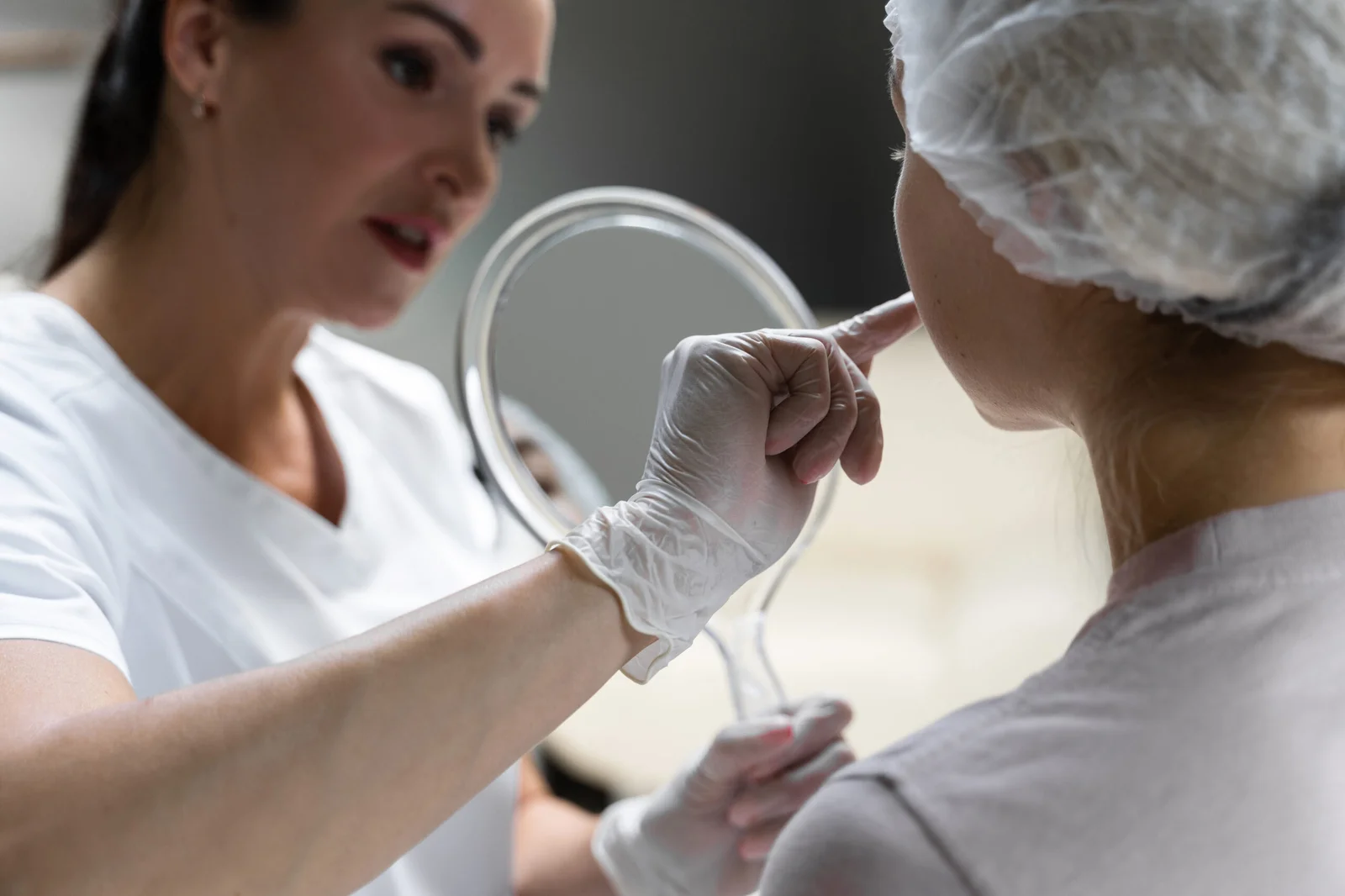 Aesthetician analysing client's skin with a hand mirror
