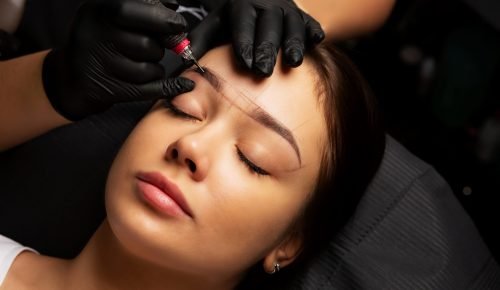 Beautician in gloves applying permanent brow makeup to a lovely brunette woman. Closeup shot
